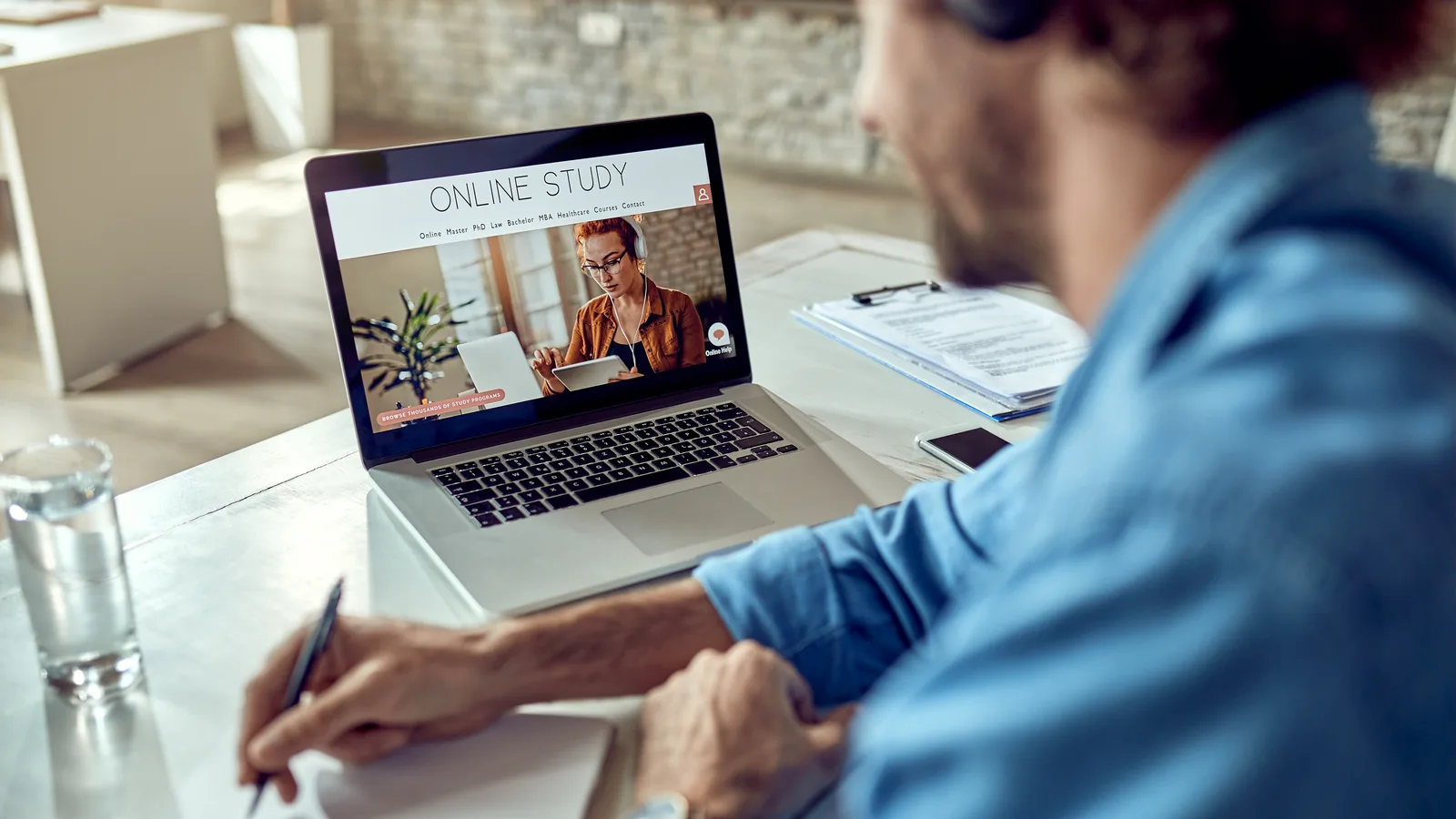 Ofisinde bilgisayarı başında oturan çalışan, ekrandaki online KVKK farkındalık eğitimi videosunu izleyip not alıyor — KVKK paketi Ofisinde bilgisayarı başında oturan çalışan, ekrandaki online KVKK farkındalık eğitimi videosunu izleyip not alıyor